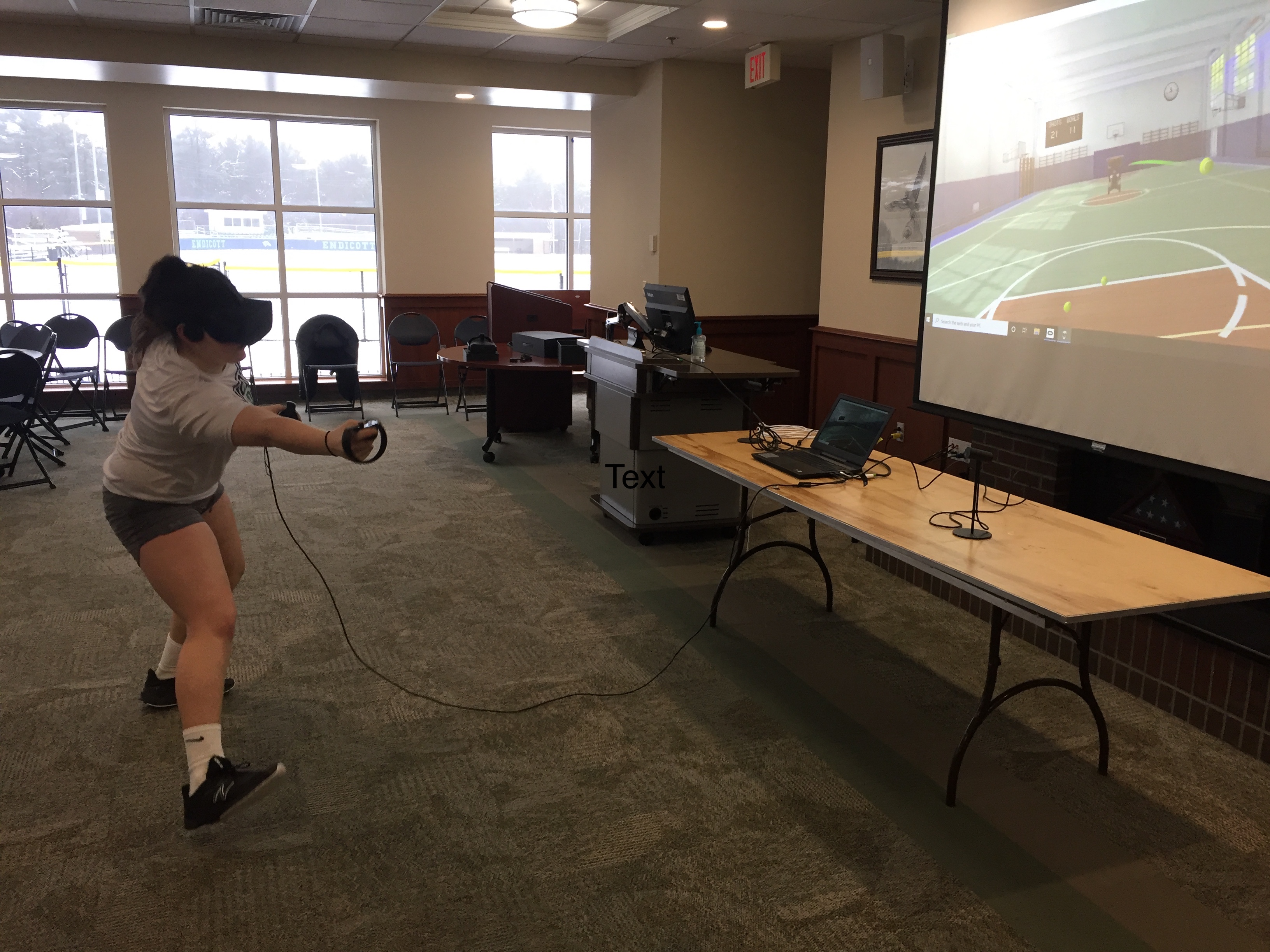 A female lacrosse player wearing a VR headset and holding controllers moves to react in a VR immersive game.