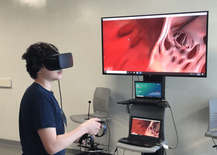 Biology student wearing a VR headset and holding controllers immersed in a close-up view of internal organs in Sharecare VR.