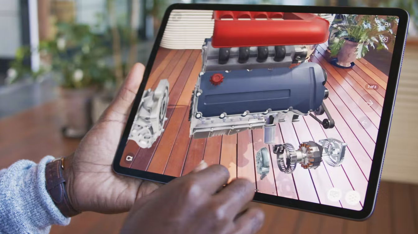 A person holds an iPad showing a 3D model of a deconstructed engine.